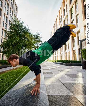Showcasing impressive athleticism, parkrunner balances on hands , framed by towering city buildings, embodying spirit of parkrun. 117195527