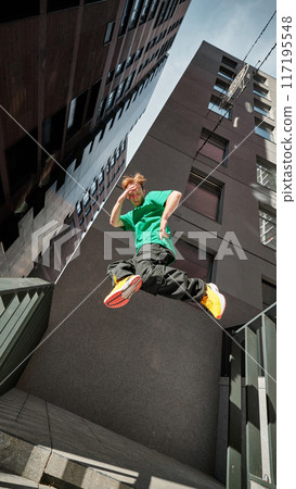 Parkrunner flips high, framed by modern city buildings, capturing exhilarating spirit and dynamic energy of modern life. 117195548