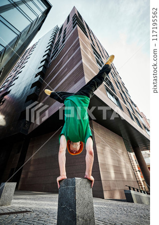 Breakdancer performs impressive handstand flip against modern urban backdrop, showcasing skills and athleticism in air. Breakdancer performs impressive handstand flip against modern urban backdrop, showcasing skills and athleticism in air. 117195562