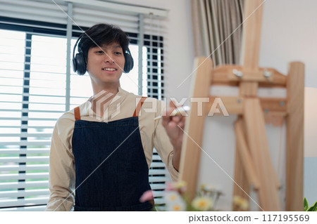 Young Artist Painting on Canvas with Headphones in Modern Studio Young Artist Painting on Canvas with Headphones in Modern Studio 117195569