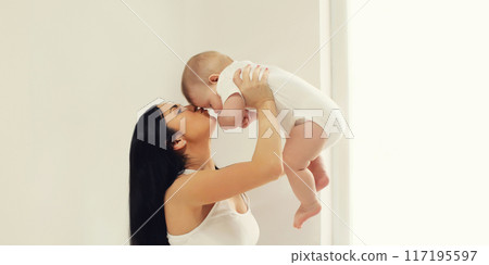 Happy young mother holds and kisses baby in white room at home 117195597