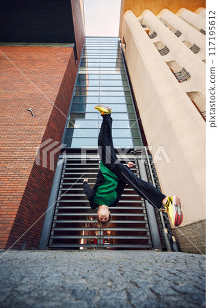 Breakdancer flips upside down, his bright yellow sneakers contrasting against towering buildings and creating dynamic visual. 117195612