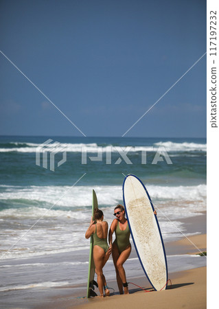 Two beautiful blondes in swimsuits pose with surfboards on the beach 117197232