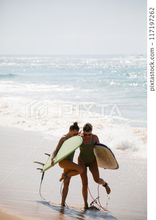 Two beautiful blondes in swimsuits pose with surfboards on the beach Two beautiful blondes in swimsuits pose with surfboards on the beach 117197262