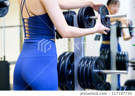 A woman's back and buttocks working out at the gym, barbell plate, weight selection, women doing muscle training, workout A woman's back and buttocks working out at the gym, barbell plate, weight selection, women doing muscle training, workout 117197730