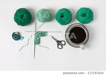 Composition of homemade needlework from cup of black coffee, scissors, mint ball for knitting and knitting needles, centimeter, pin. Hobbies of knitting warm clothes, toys, things for house. Composition of homemade needlework from cup of black coffee, scissors, mint ball for knitting and knitting needles, centimeter, pin. Hobbies of knitting warm clothes, toys, things for house. 117197824
