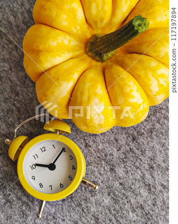 Bright yellow pumpkin and matching yellow alarm clock placed on gray surface, showcasing vibrant colors and cozy autumn vibes Bright yellow pumpkin and matching yellow alarm clock placed on gray surface, showcasing vibrant colors and cozy autumn vibes 117197894