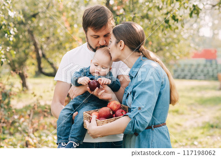 Young family with a baby enjoying apple picking in an orchard, holding a basket of apples. the joy and togetherness of family time in nature. Young family with a baby enjoying apple picking in an orchard, holding a basket of apples. the joy and togetherness of family time in nature. 117198062