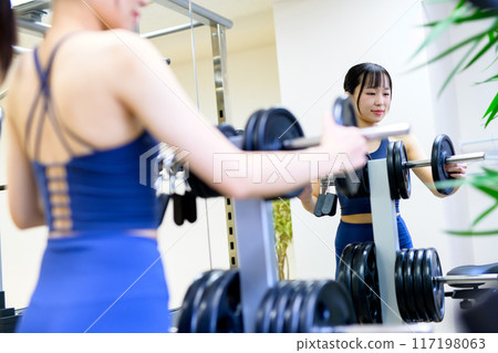 The back of a woman working out at the gym, barbell plate, weight selection, women doing muscle training, workout 117198063