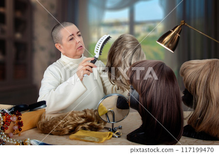 Intimate Moment of Self-Care: Woman Focuses on Combing Gray Wig in Cozy Home with Additional Wigs on Display Intimate Moment of Self-Care: Woman Focuses on Combing Gray Wig in Cozy Home with Additional Wigs on Display 117199470