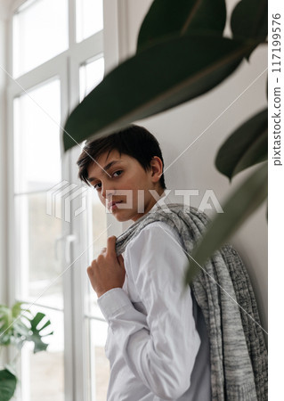 portrait of a pretty teenager standing near the window indoors and looking at camera portrait of a pretty teenager standing near the window indoors and looking at camera 117199576