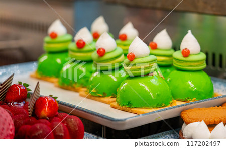 Macarons on sponge cake covered with green icing and whipped cream 117202497