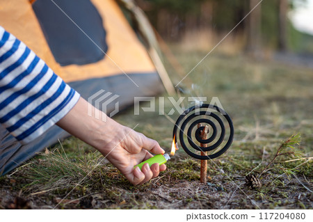 Hand with lighter igniting repellent coil - fumigator with smoke for repelling insects in nature Hand with lighter igniting repellent coil - fumigator with smoke for repelling insects in nature 117204080