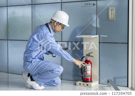 一名穿著工作服的男子檢查滅火器,建築物維護圖像 一名穿著工作服的男子檢查滅火器,建築物維護圖像 117204705