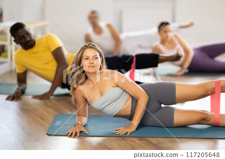 Pilates class - group of people of different nationalities doing leg stretches using resistance bands 117205648