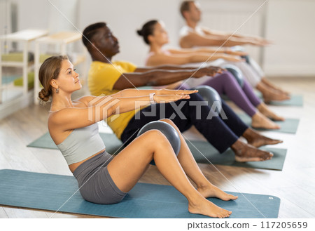 Multiethnic group of people doing exercises for press with pilates ball during group class in fitness gym Multiethnic group of people doing exercises for press with pilates ball during group class in fitness gym 117205659