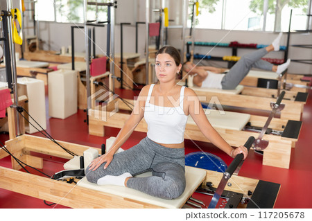 Active young woman doing arm exercises on reformer device Active young woman doing arm exercises on reformer device 117205678
