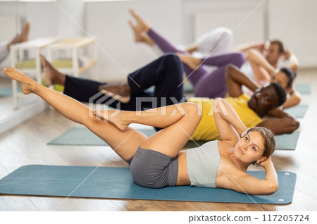 Multinational Pilates participants pulls elbows up to opposite knee, performs exhausting exercises Multinational Pilates participants pulls elbows up to opposite knee, performs exhausting exercises 117205724