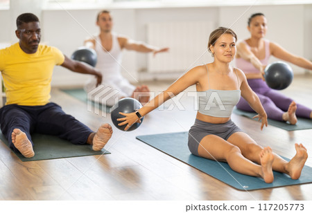Young female Pilates instructor exercising with ball during group class Young female Pilates instructor exercising with ball during group class 117205773