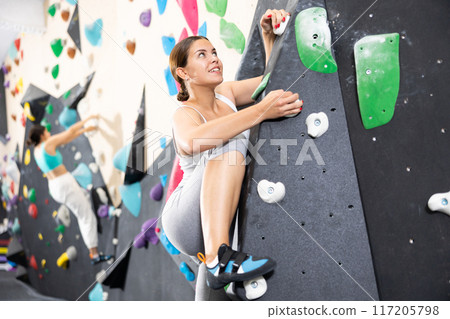 Young Europian woman climbs steep artificial wall in sports complex and trains endurance Young Europian woman climbs steep artificial wall in sports complex and trains endurance 117205798