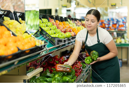 Female seller in apron chooses juicy bell pepper 117205865