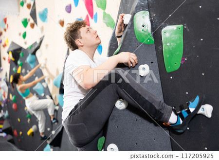 Teenage boy climbs steep artificial wall in sports complex and trains endurance Teenage boy climbs steep artificial wall in sports complex and trains endurance 117205925