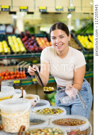Young woman putting olives in plastic packaging in grocery store Young woman putting olives in plastic packaging in grocery store 117205945