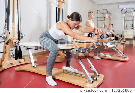 Young woman stretching her arms using pilates machine Young woman stretching her arms using pilates machine 117205996
