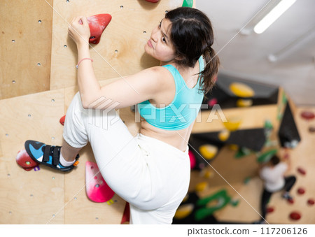 Sporty woman exercising on wall in climbing gym during bouldering training 117206126