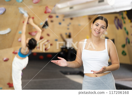 Smiling young girl posing near climbing wall at bouldering gym after workout, feeling accomplished and energized 117206168