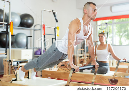 Young guy doing full body exercises lying on reformer device 117206170
