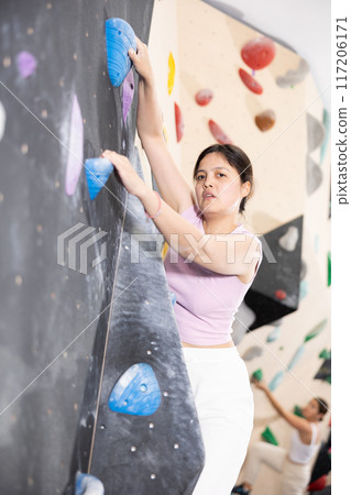 Young Asian woman climbs steep artificial wall in sports complex and trains endurance Young Asian woman climbs steep artificial wall in sports complex and trains endurance 117206171