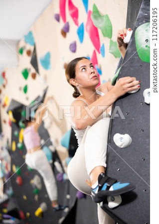 Europian girl focused on climbing to top of artificial bouldering wall along complicated route track Europian girl focused on climbing to top of artificial bouldering wall along complicated route track 117206195