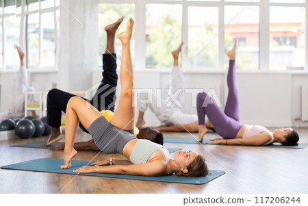 Gir doing single leg bridge during group pilates session 117206244