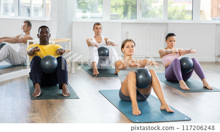 Young female Pilates instructor performing sit-ups with ball at group class Young female Pilates instructor performing sit-ups with ball at group class 117206248