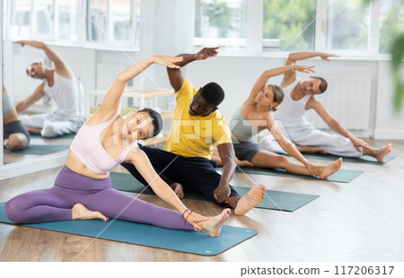 Young Asian teacher working out Parivritta Janu Shirshasana with multinational students group Young Asian teacher working out Parivritta Janu Shirshasana with multinational students group 117206317