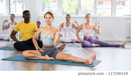 Young woman with multinational people performs stretches elastic band with hand and foot 117206329
