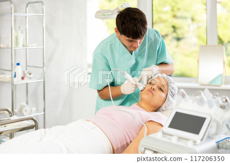Young male cosmetologist doing ultrasound procedure to young woman Young male cosmetologist doing ultrasound procedure to young woman 117206350