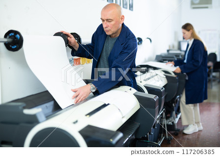 Service man uses plotter and checks functionality in printing shop 117206385