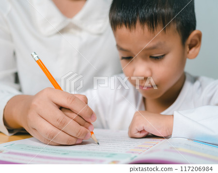 Teacher or mother helping boy writing lesson and learning to write, Education home school concept, Female tutor helping little elementary school boy with homework during individual lesson at home 117206984