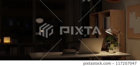 A modern dark office at night, a laptop and accessories on a desk, illuminated by a table lamp. 117207047
