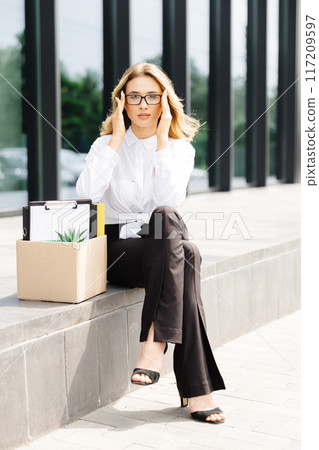 Caucasian businesswoman walking outdoors with box of stuff leaving business. Female office worker lost her job. Fired woman coming back home Caucasian businesswoman walking outdoors with box of stuff leaving business. Female office worker lost her job. Fired woman coming back home 117209597
