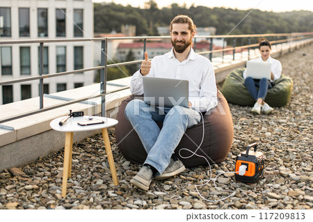 Business man working outdoors on rooftop with laptop and portable power station 117209813