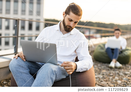 Business man connects charging cable to laptop outdoors 117209829