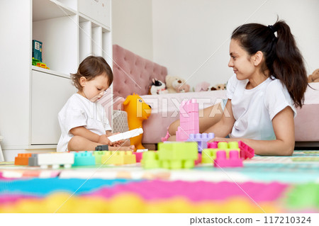 cute baby girl and her loving mother playing with toy bricks in the children room, early development 117210324