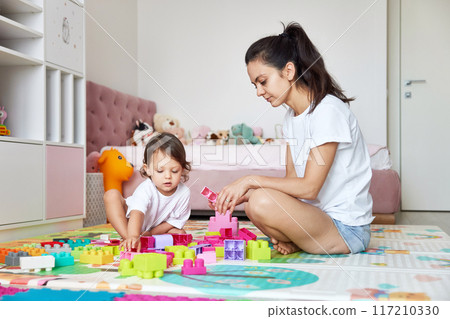cute little baby girl and her mom playing with colorful blocks in the children room, having fun together 117210330