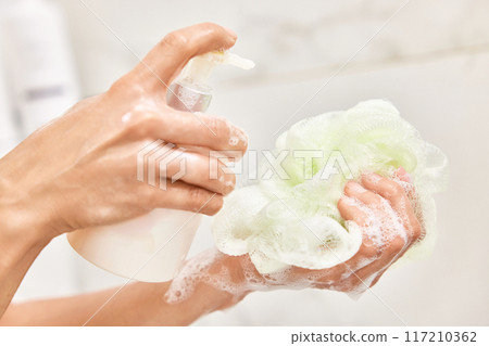 female hands applying liquid soap shower gel from white cosmetic bottle on sponge in bathroom female hands applying liquid soap shower gel from white cosmetic bottle on sponge in bathroom 117210362