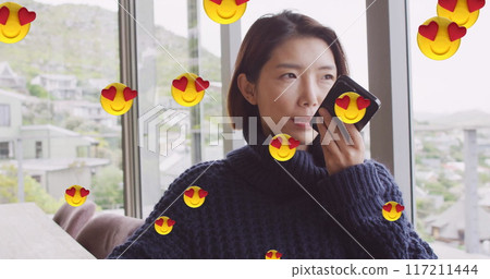 Image of emoji icons over asian woman using smartphone at home 117211444