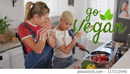 Image of go vegan text over gay lesbian couple dancing and cooking together at home 117212040