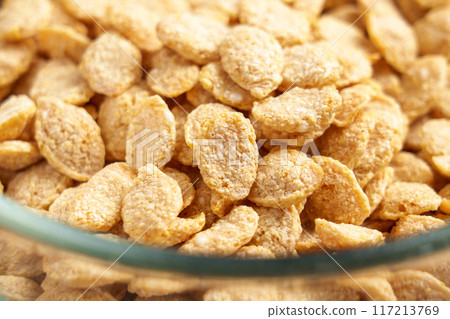Crispy breakfast cereal flakes in the form of grains in a glass transparent kitchen bowl close up. Organic nutritional food.  117213769